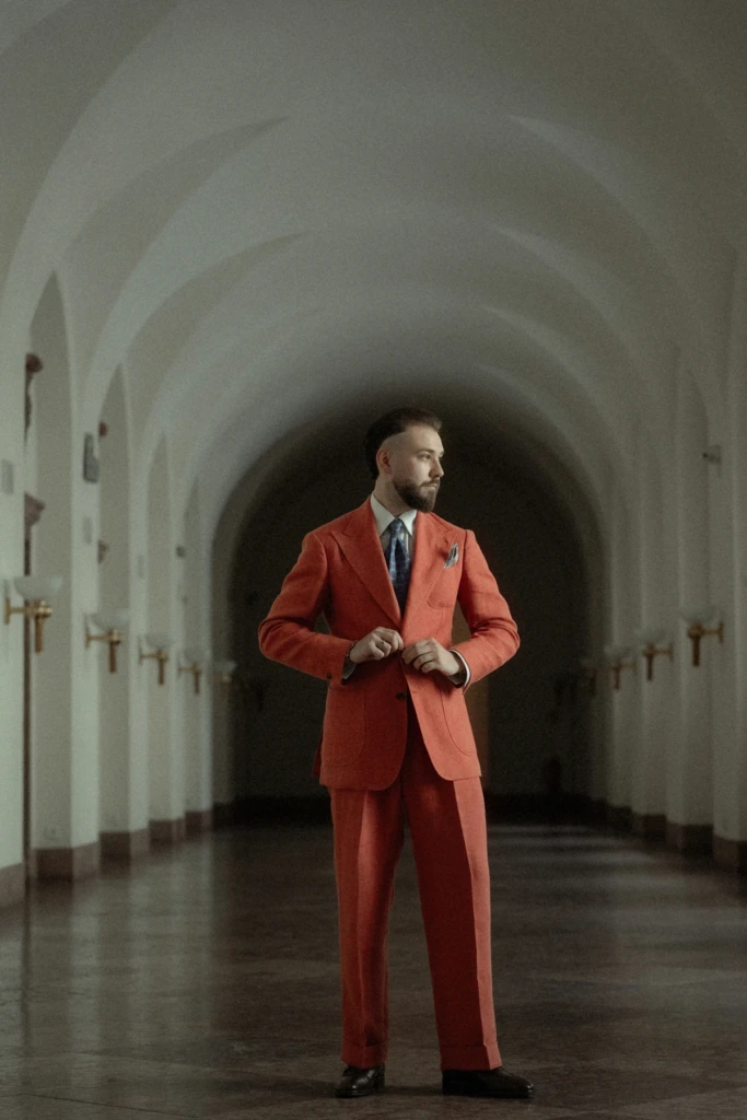 Cała sylwetka męska w pomarańczowym garniturze lnianym, zamkowe wnętrze, styl elegancki, boho.