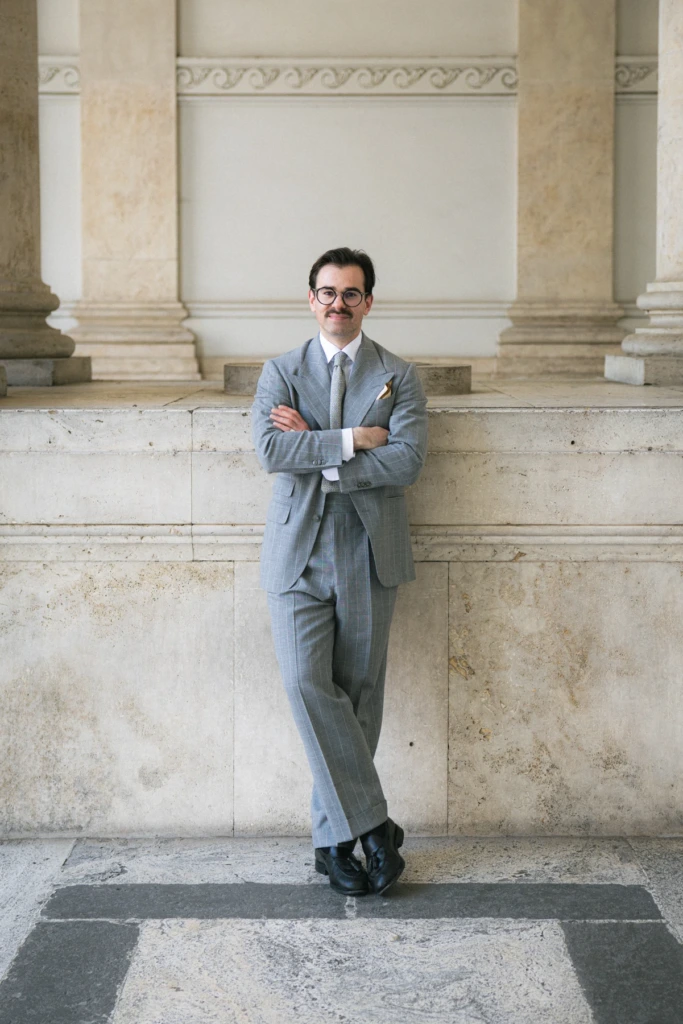 Szary garnitur w prążki w kroju vintage, biała koszula winchester w szałwiowe pasy, czarne buty tassel loafers, jasne tło.