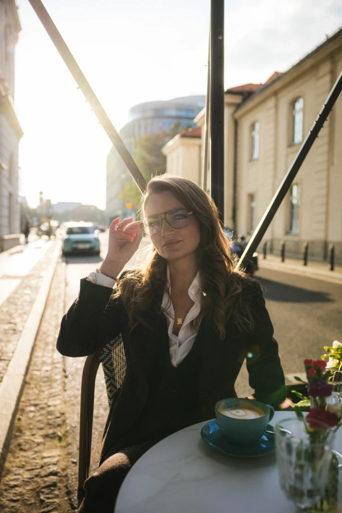 Kobieta w brązowym flanelowym garniturze z białą koszulą, przy stole, pijąca kawę.